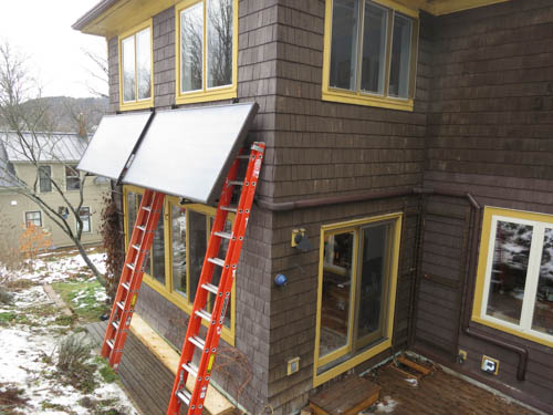 The wall-mounted collectors being installed on the back wall of our house. Glycol is pumped through the panels via the piping along the side of the house.